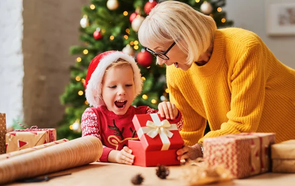 圣诞佳节期间 戴着圣诞礼帽的孩子兴奋地打开奶奶送给他的礼物盒 — 图库照片