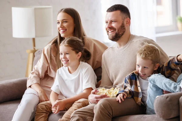 楽しい家族の両親と子供はポップコーンを食べて ソファに座っている間に笑って 家で面白い映画を見て — ストック写真