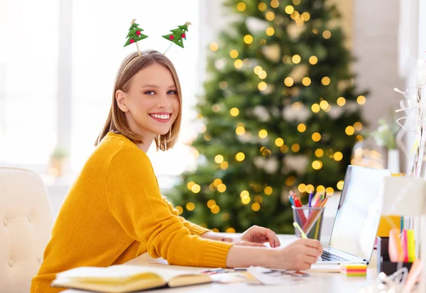 幸せなかなり面白い女の子フリーランサー笑顔 ラップトップでリモートで作業し クリスマス前に自宅でメモを取る — ストック写真