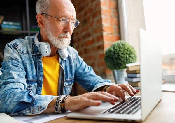 穿着时髦衣服的年长男性自由职业者在笔记本电脑键盘上打字 一边坐着写字台一边在家里工作 — 图库照片