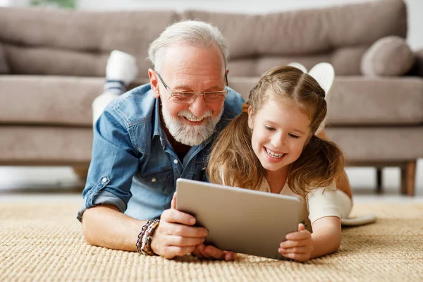 周末的一天 快乐的家人 爷爷和女儿躺在地板上 在平板电脑上看卡通片 — 图库照片