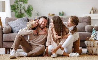 Mutlu aile, anne, baba ve çocuklar evde, yerde, solun yanında.