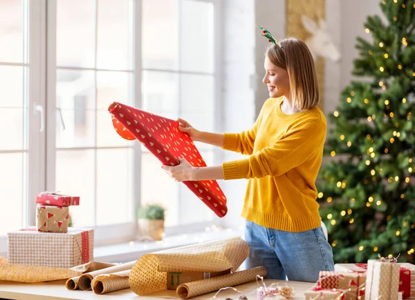 幸せな若い女性笑顔と贈り物のための包装紙を選択しながら 自宅でクリスマスのお祝いの準備 — ストック写真