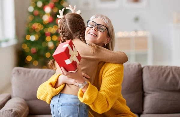 Χαριτωμένο Κορίτσι Αγκαλιάζει Χαρούμενη Ηλικιωμένη Γυναίκα Κάθεται Στον Καναπέ Χριστουγεννιάτικο — Φωτογραφία Αρχείου