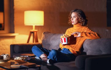 Şaşkın genç bir kadın patates kızartması yiyor ve akşam TV 'de heyecan verici aksiyon dolu bir film izliyor.