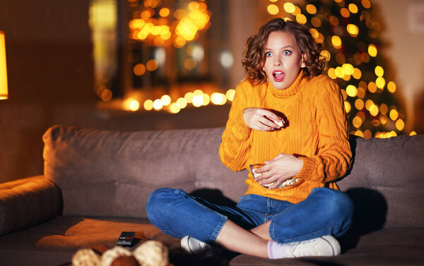 young surprised dumbfounded woman eating popcorn and watches an exciting action-Packed movie on TV at home in evening  alon