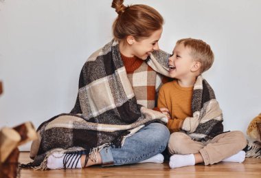 Mutlu aile annesi ve sevgili oğlu sıcak bir kış akşamında sıcak bir battaniyeye sarılıp gülüyorlar.