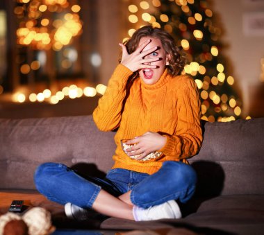 Şaşırmış bir kadın yüzü patlamış mısırla kaplı ve geceleri evde kanepede otururken korku filmi seyrediyor.