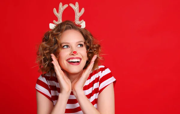 楽しいです面白いです若いです女性でクリスマストナカイの衣装笑いと上を見上げますカラフルな赤い背景 — ストック写真