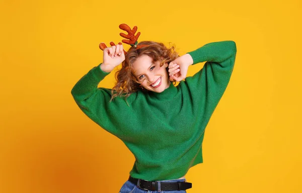 穿着圣诞绿色毛衣 头戴鹿角的快乐而有趣的年轻女人 穿着黄色的背带舞 享受着生活 — 图库照片