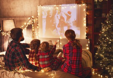 Kareli pijamalı mutlu aile: Anne baba ve çocuklar projektör, film, evde patlamış mısırlı filmler izliyor.