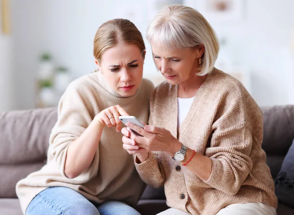 Bewildered Mother Daughter Frowning Browsing Smartphone While Sitting Couch Home — Stock Photo, Image