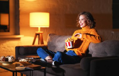 Mutlu kadın, örgü kazak giyip patates kızartması yerken ve ilginç bir film izlerken akşam evde kanepede bacak bacak bacak üstüne atarak oturuyor.