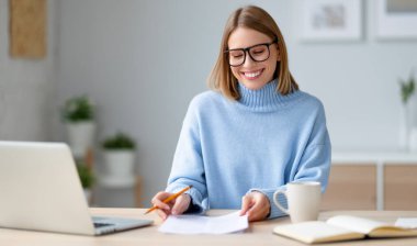Mutlu genç bayan serbest çalışan gülümseyen ve kağıtları incelerken masada oturup evdeki uzak projede çalışıyor.