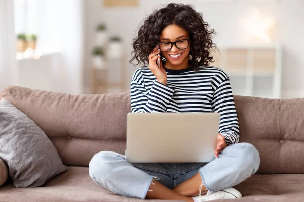 Mujer Étnica Feliz Usando Ordenador Portátil Hablando Teléfono Inteligente Mientras — Foto de Stock