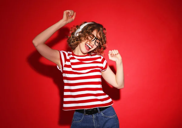 ヘッドフォンで音楽を聴きながら 赤い背景に目を閉じて踊るカジュアルな服を着た興奮した若い女性 — ストック写真