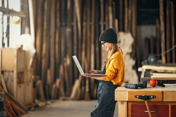 年轻的女木匠在现代手工艺工作室用木料工作时 在笔记本电脑上看图画 — 图库照片