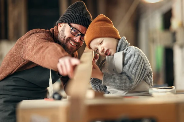 快乐的家庭小男孩和爸爸 身穿毛衣 头戴帽子 手执木板 一起在现代手工艺工作室工作 — 图库照片