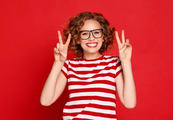 赤を背景にVサインを示すスタイリッシュなストライプTシャツで楽しい若い女性 — ストック写真