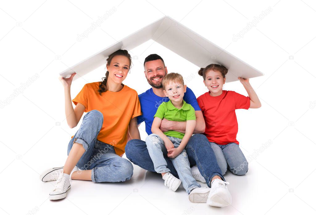 Delighted couple with kids sitting under paper roof in studio on white background while looking at camera and showing concept of relocation and new home