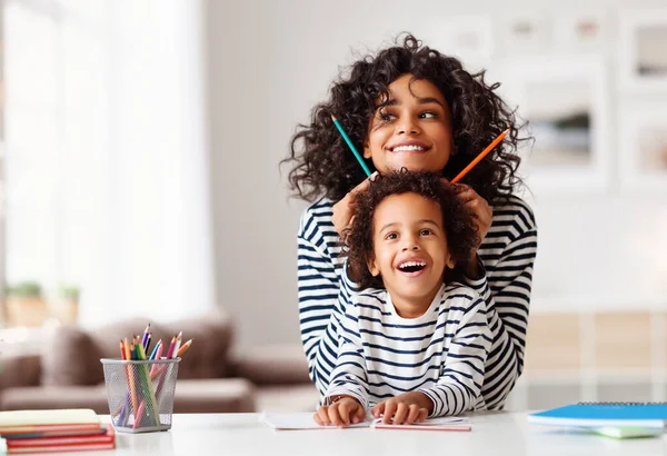 テーブルに座って家で宿題をしている間にアフリカ系アメリカ人の家族の女性と男の子が鉛筆で笑ったり遊んだり — ストック写真