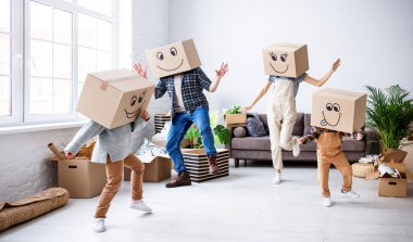 Carefree parents and kids in carton boxes on heads dancing in new spacious flat while having fun and enjoying relocation together clipart