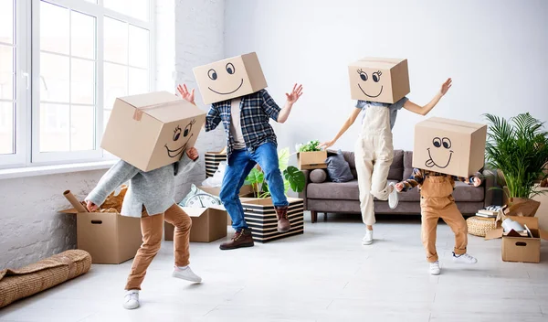 Carefree parents and kids in carton boxes on heads dancing in new spacious flat while having fun and enjoying relocation together