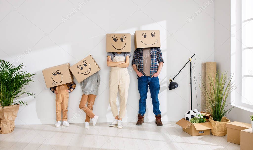 Unrecognizable family: couple and kids wearing carton boxes on heads standing near wall in new spacious apartment during relocation