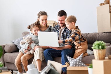 Mutlu bir aile, yeni bir eve taşınırken birlikte kanepede oturup dizüstü bilgisayarlarına bakarlar.