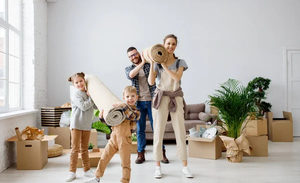 Joyful family: content couple and cheerful kids with carpets standing in new apartment and looking at camera during relocation