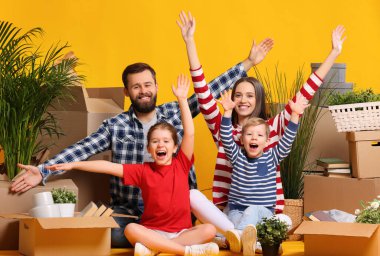 Mutlu bir aile: Ebeveynler ve çocuklar yeni bir daireye taşındıktan sonra kutuların arasında birlikte otururken eğleniyor ve kollarını kaldırıyorlar.
