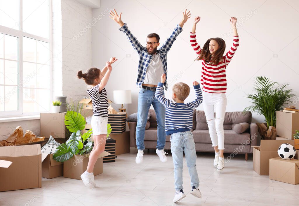 Full length excited parents and kids raising arms and leaping up near carton boxes while celebrating relocation into new apartment
