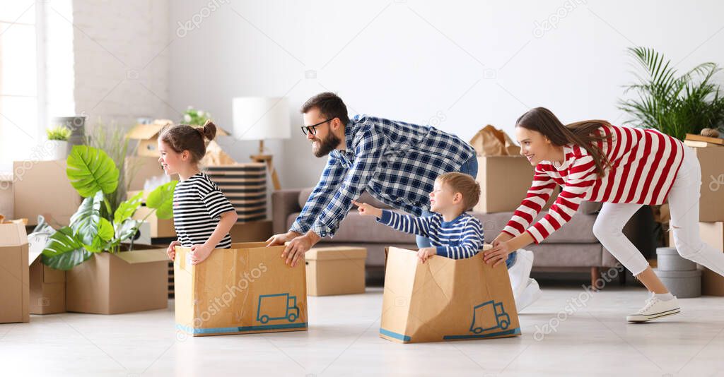 Playful family: parents riding kids in boxes and having fun during moving in new spacious apartment