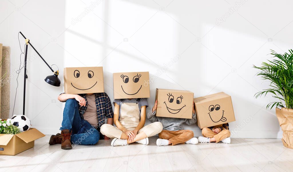 Unrecognizable family: couple and kids wearing carton boxes on heads sitting near wall in new spacious apartment during relocation