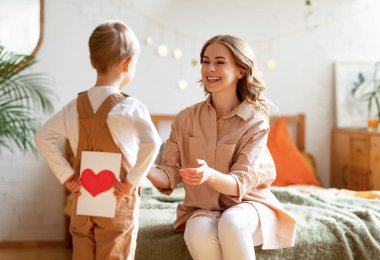 Arkasında kalp olan el yapımı tebrik kartı saklayan çocuk yatak odasında mutlu anneyi tebrik ediyor.