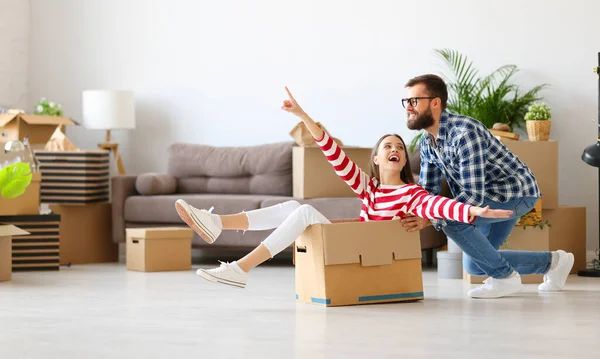 Full body side view of positive family couple young man pushing carton box with laughing woman while having fun together during unpacking things in new home