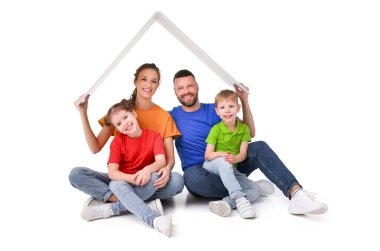 Kameraya bakarken, taşınma ve yeni ev kavramını gösterirken çocukları olan mutlu çift beyaz arka planda kağıt çatı altında oturuyor.