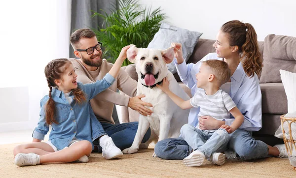 Happy playful parents and kids having fun and playing with cute dog while gathering together on floor in living room during weekend at home