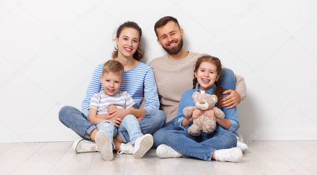 Full body of cheerful family with little kids looking at camera while sitting together on floor near wall in empty room of new home