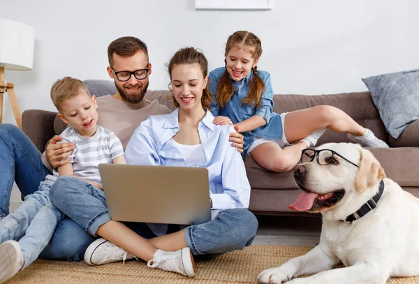 小さな子供と面白いラブラドールの検索犬を持つ陽気な家族は ノートパソコンの周りに集まり 家で一緒に自由な時間を過ごしながら面白い映画を見ています — ストック写真