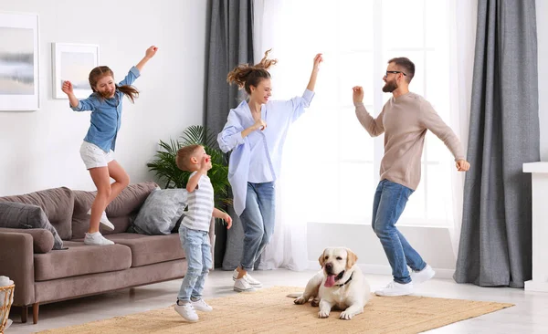 Full body of happy energetic family: parents and kids having fun and dancing while cute tired dog resting on carpet during weekend at home