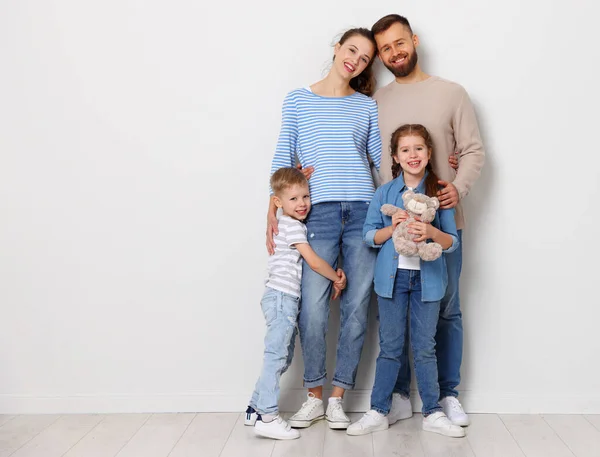 Full body of cheerful family with little kids looking at camera while standing together on floor near wall in empty room of new home