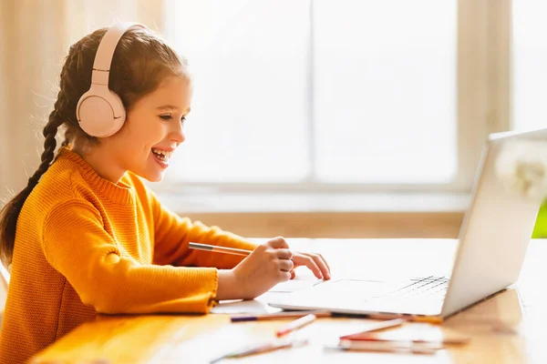 Positive Little Schoolgirl Headphones Communicating Tutor Making Notes Copybook Online — Stock Photo, Image