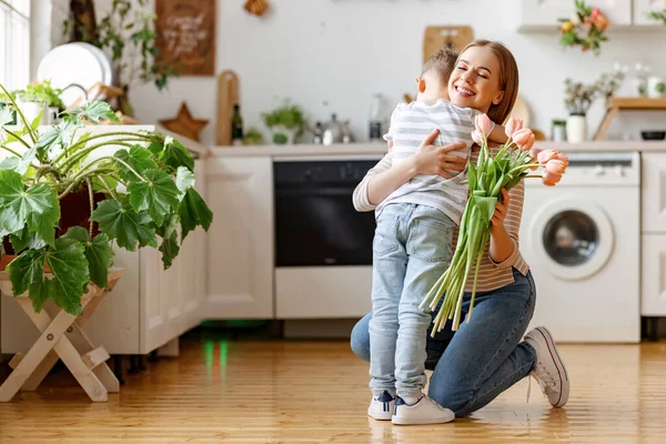 Happy adult woman with tulips smiling with closed eyes and embracing boy in gratitude while celebrating holiday mothers day at home