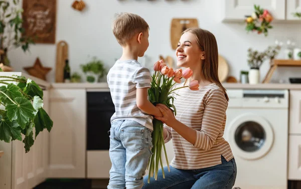 즐거운 소년이 집에서 어머니를 축하하는 어머니를 어머니에게 꽃다발을 — 스톡 사진