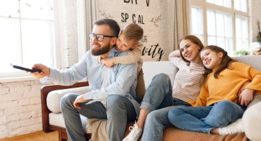 Mutlu aile babaları ve çocuklar kanepede oturup TV izlerken gülümsüyor.