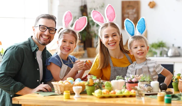 欢乐的家庭 戴着兔子耳朵的头带 聚集在现代轻便厨房的餐桌旁 一起痛苦地吃着复活节彩蛋 看着相机 — 图库照片