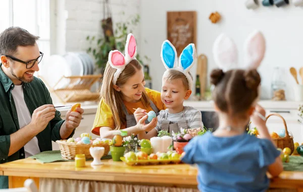 欢乐的家庭 戴着兔子耳朵的头带 聚集在现代轻便厨房的餐桌旁 一起痛苦不堪地吃复活节彩蛋 — 图库照片