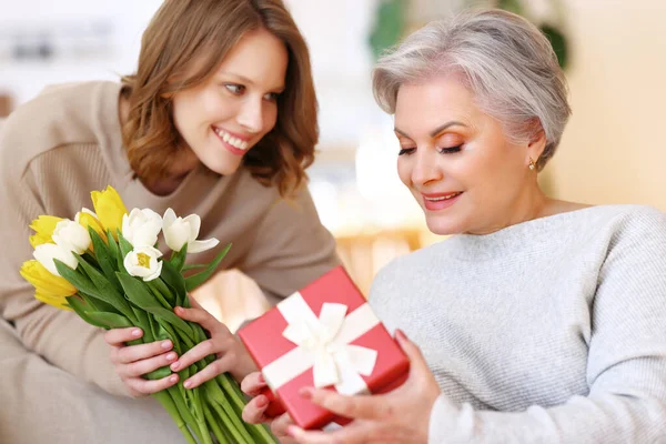 在母亲回家的日子里 快乐的年轻女性拥抱着快乐的年迈的母亲 献上一束郁金香和礼物 — 图库照片