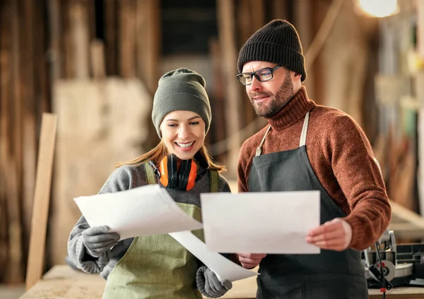 Positive männliche und weibliche Handwerksunternehmer in Schürzen diskutieren Papierentwurf bei gemeinsamer Arbeit in Tischlerwerkstatt — Stockfoto